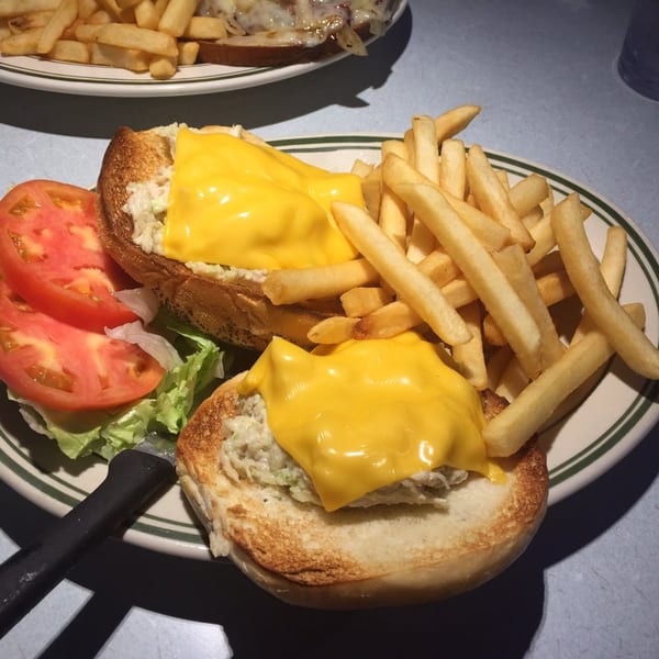 Open-faced tuna melt with melted cheese, lettuce, tomato, and a side of french fries.