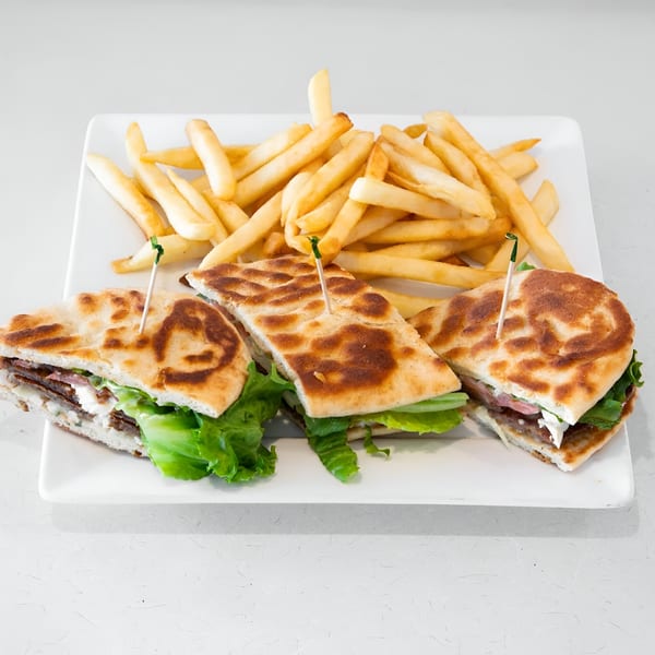 Three flatbread sandwiches with meat, lettuce, and cheese, served with a side of golden fries.