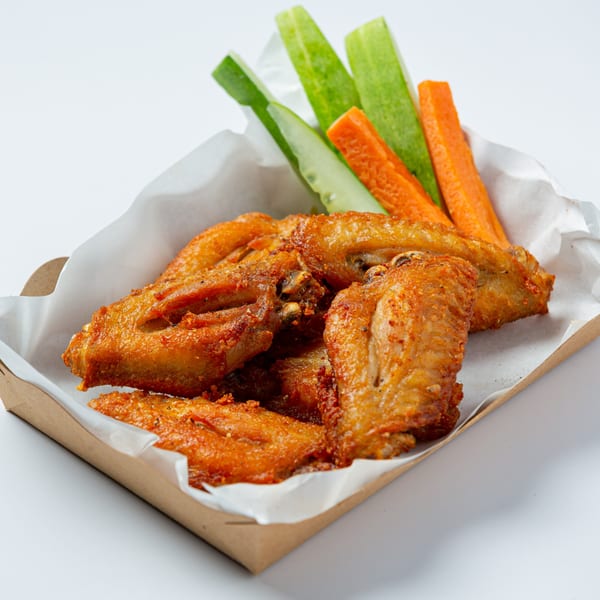 Crispy fried chicken wings with cucumber and carrot sticks in a paper-lined cardboard tray.