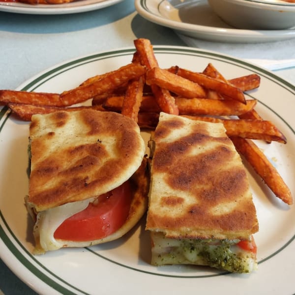 A grilled panini sandwich, cut in half, with sweet potato fries on a white plate with green stripes.
