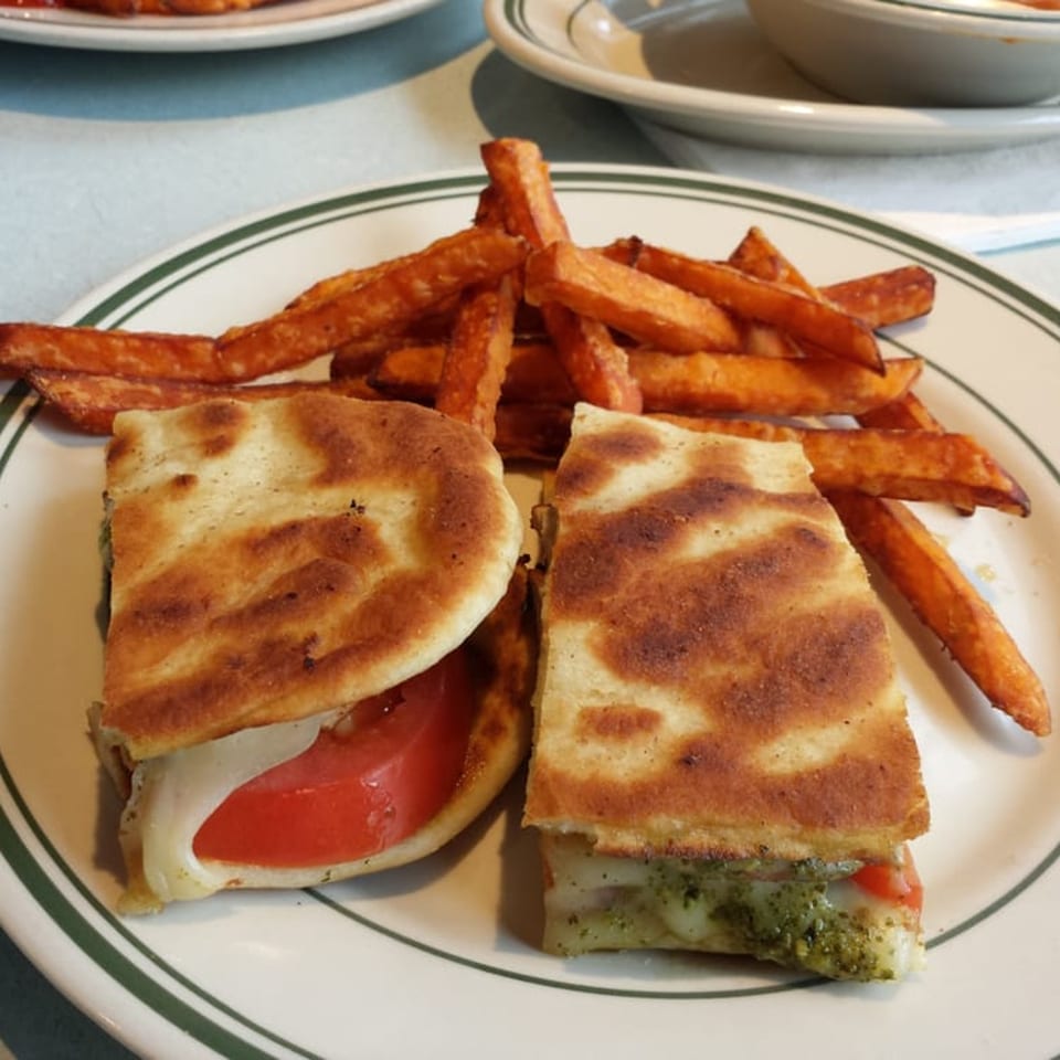A grilled panini sandwich, cut in half, with sweet potato fries on a white plate with green stripes.
