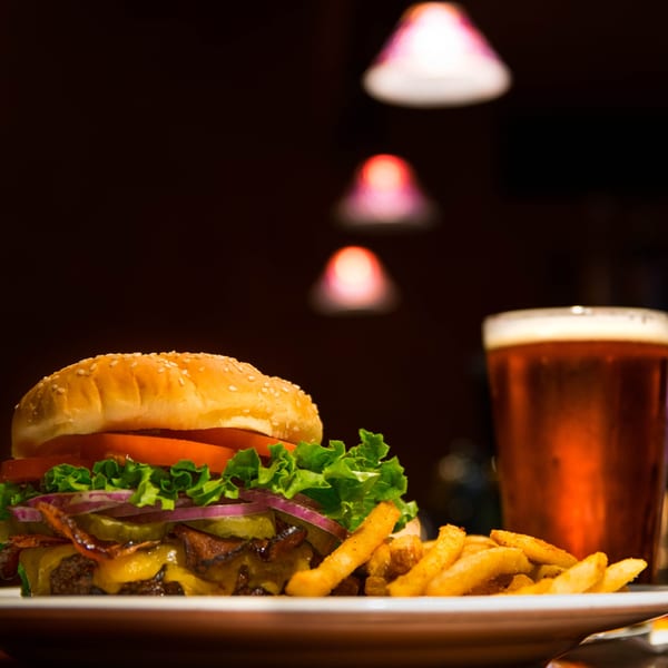 A bacon cheeseburger with fries and a glass of beer on a white plate at Yesterday's Diner.