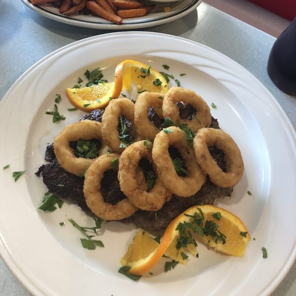 Yesterday's Diner steak topped with onion rings, garnished with parsley and orange slices.